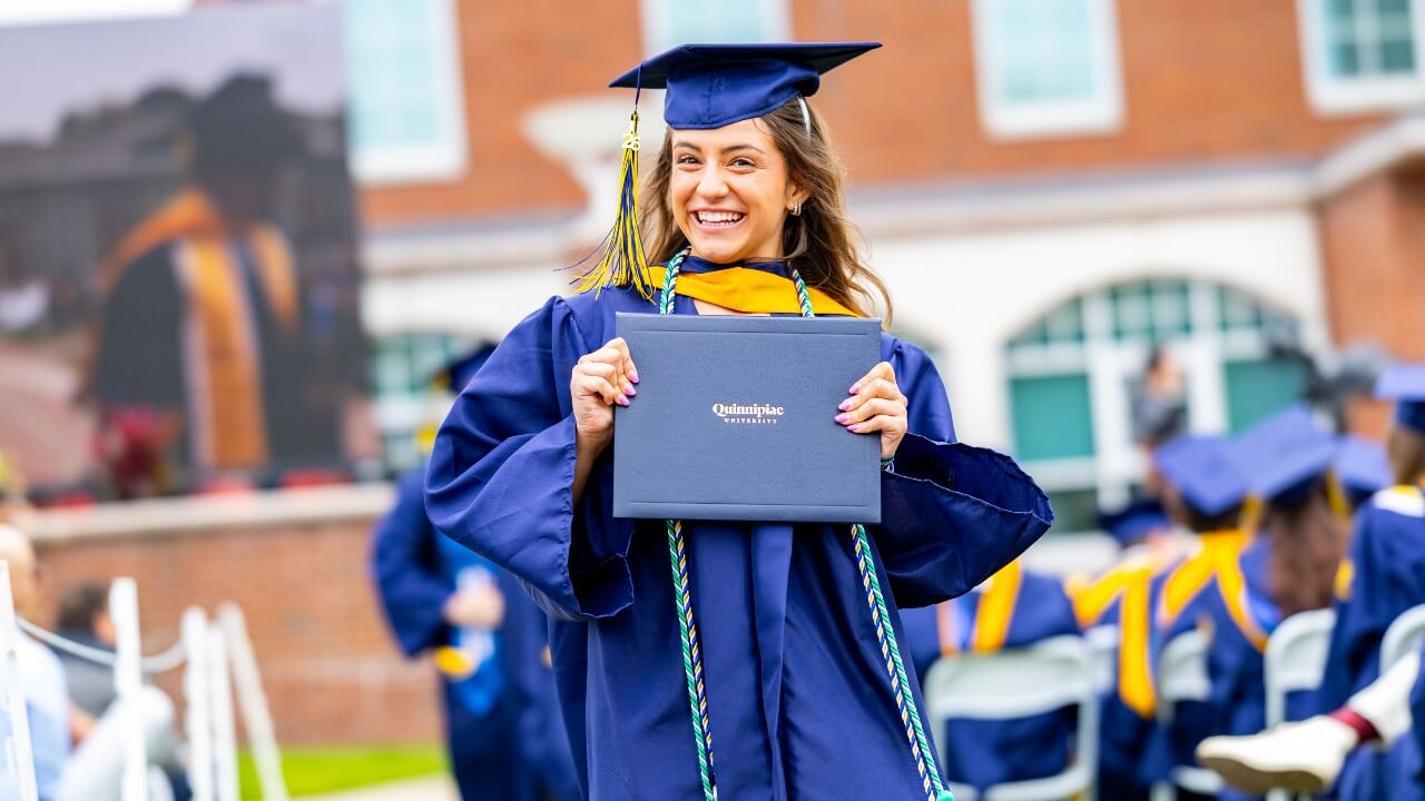 Graduate in cap and gown smiles with their diploma.