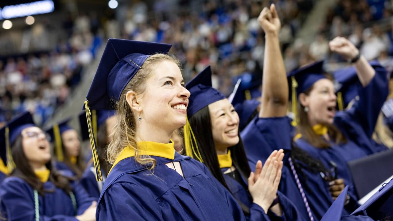 Graduate in cap and gown smiles in the crowd.