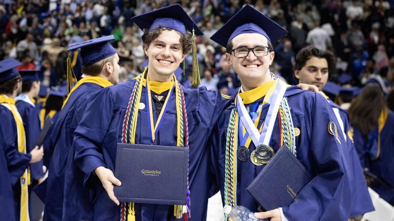 Two graduates in caps and gowns smiles for a photo.