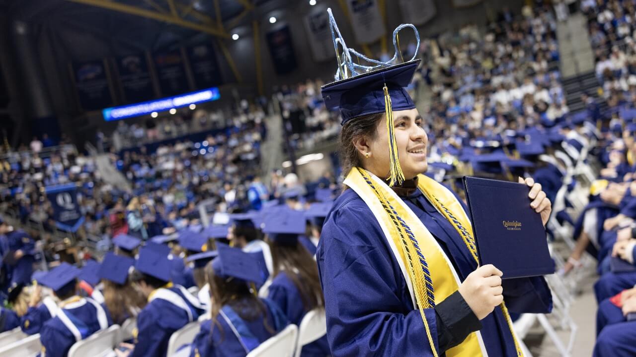 Graduate with a handcrafted rollercoaster on cap smiles with diploma