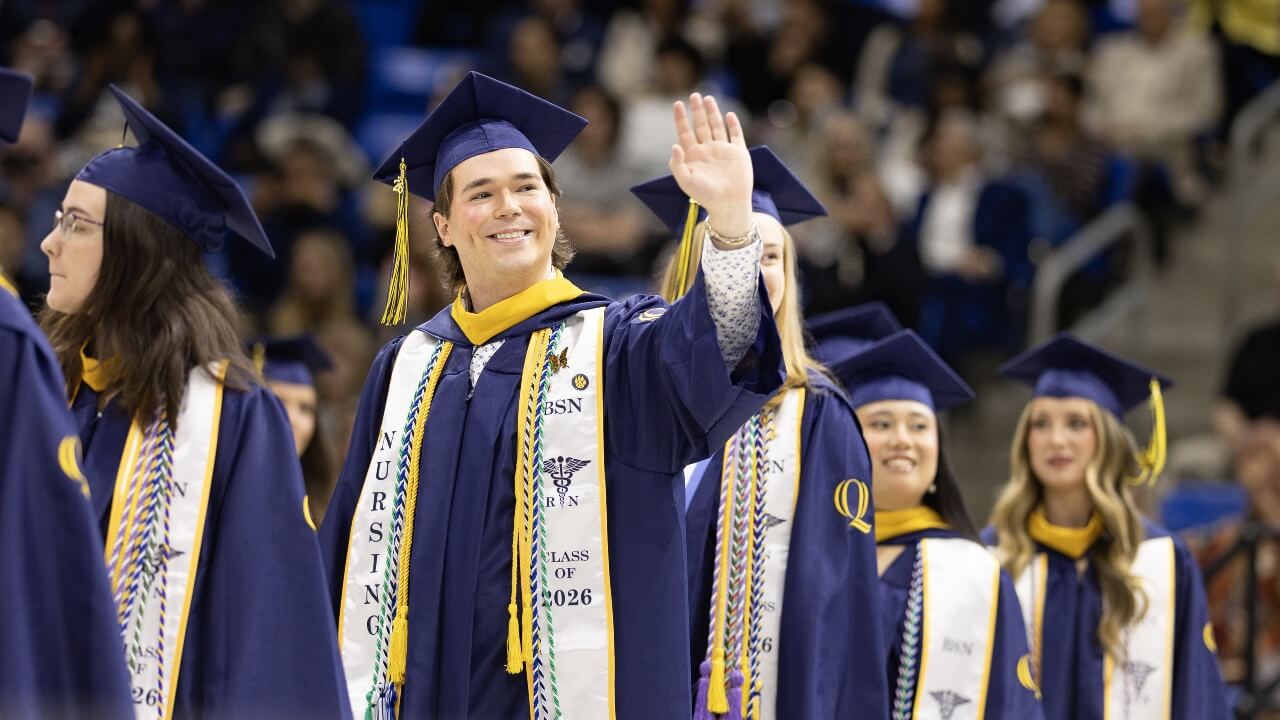 Graduates walking in a procession waving to their families