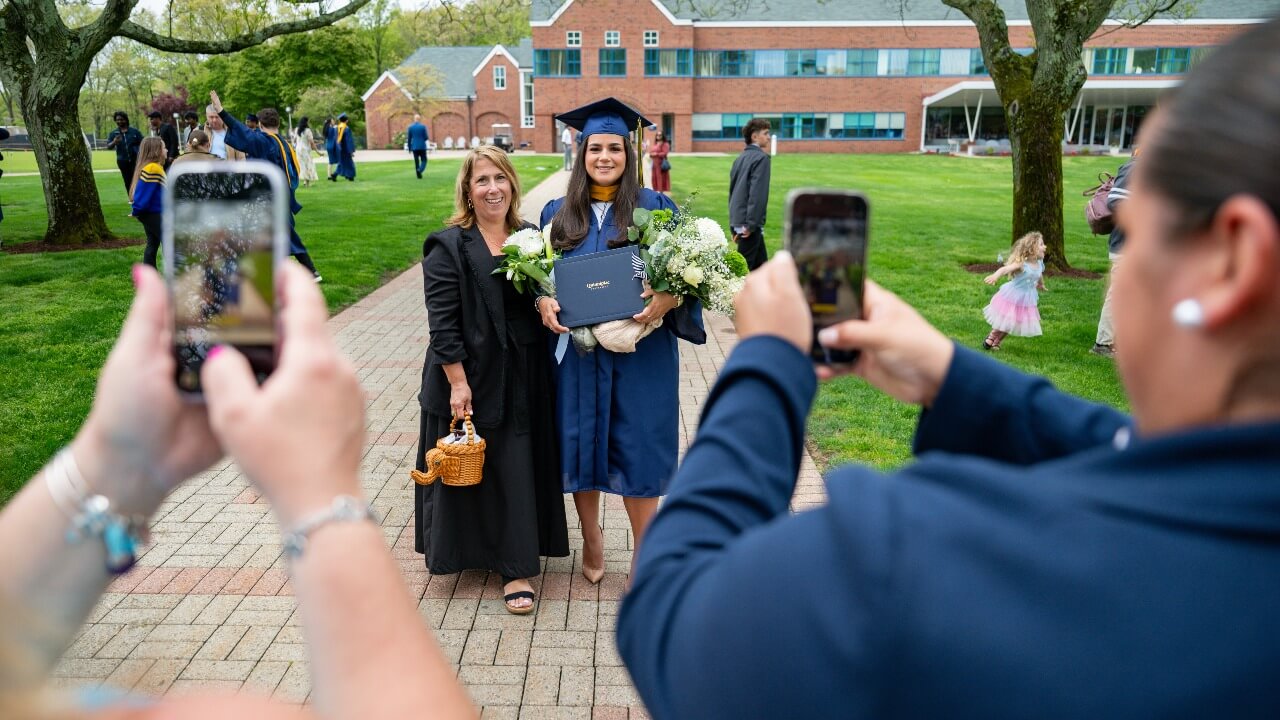 Two phones take pictures of a graduate in cap and gown with their loved ones.