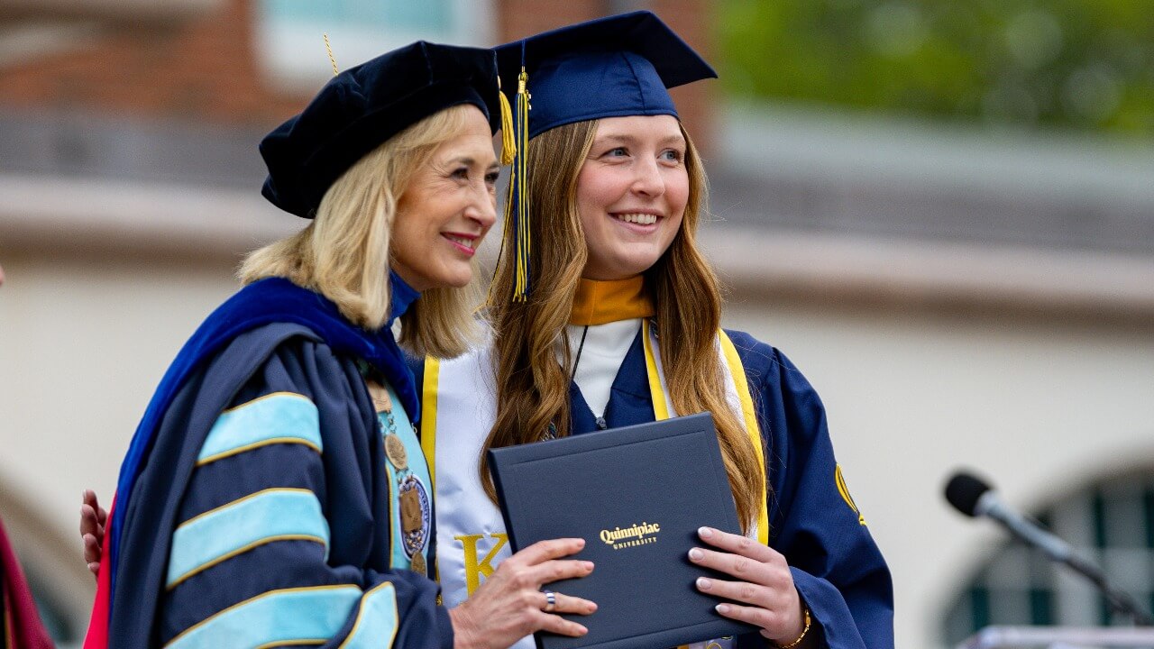Graduate in cap and gown smiles for a photo with President Marie Hardin.
