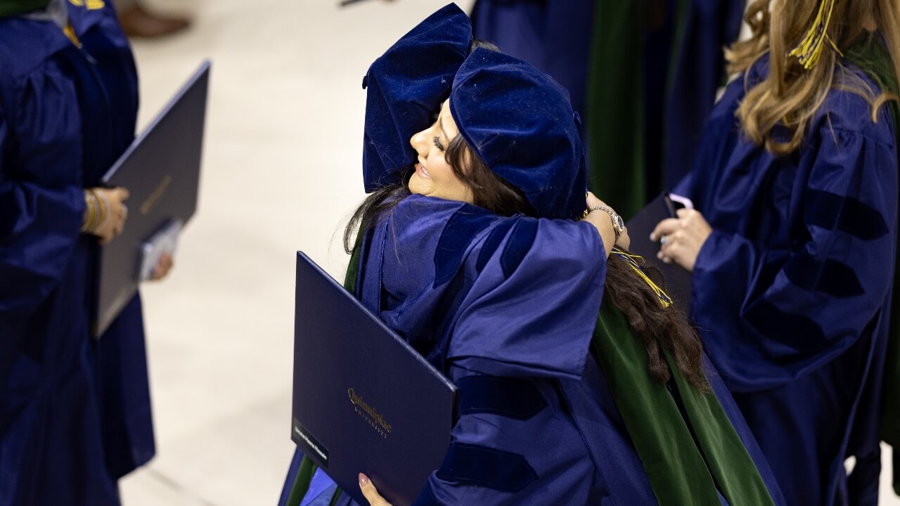 Graduate students smiling and hugging at Commencement