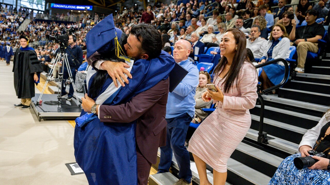 Graduate hugging their loved one at the base of the bleachers