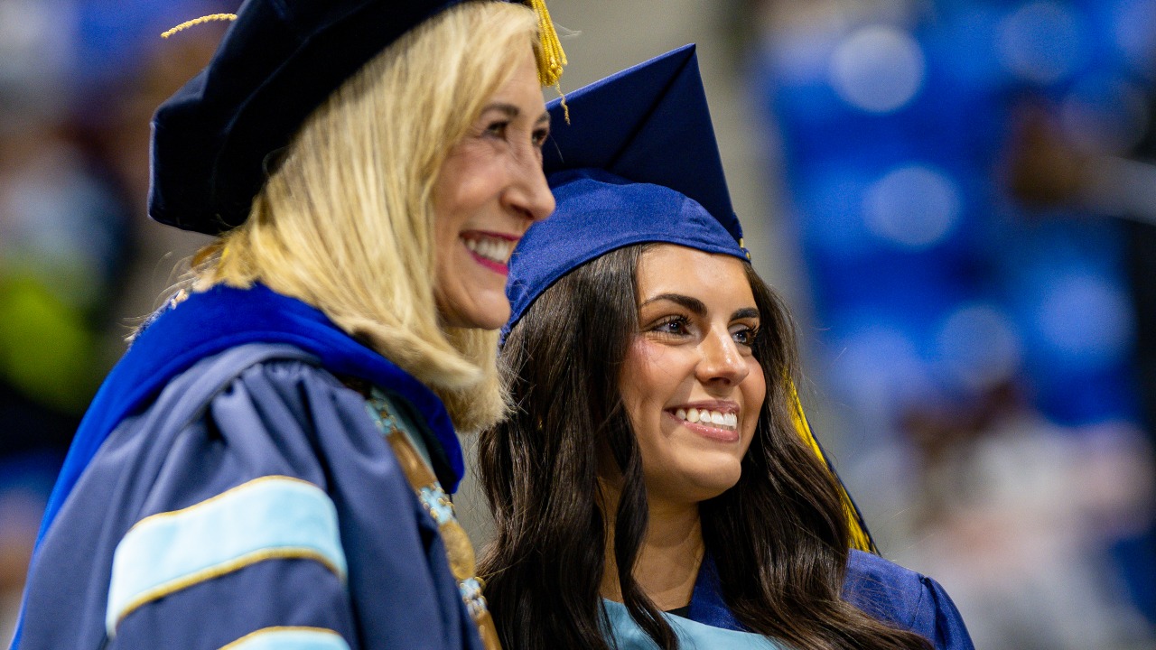 Graduate smiles with President Marie Hardin and her diploma