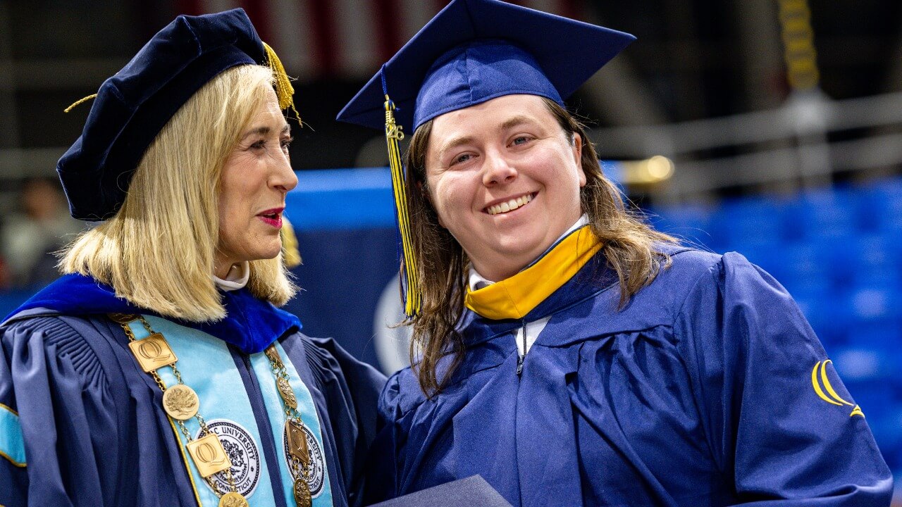 Graduate and President Hardin pose for photo on stage with diploma