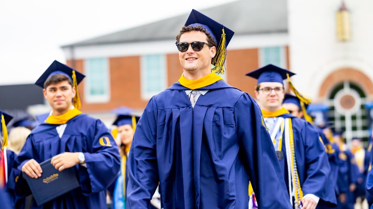 Graduate walking with peers down the aisle while wearing sunglasses