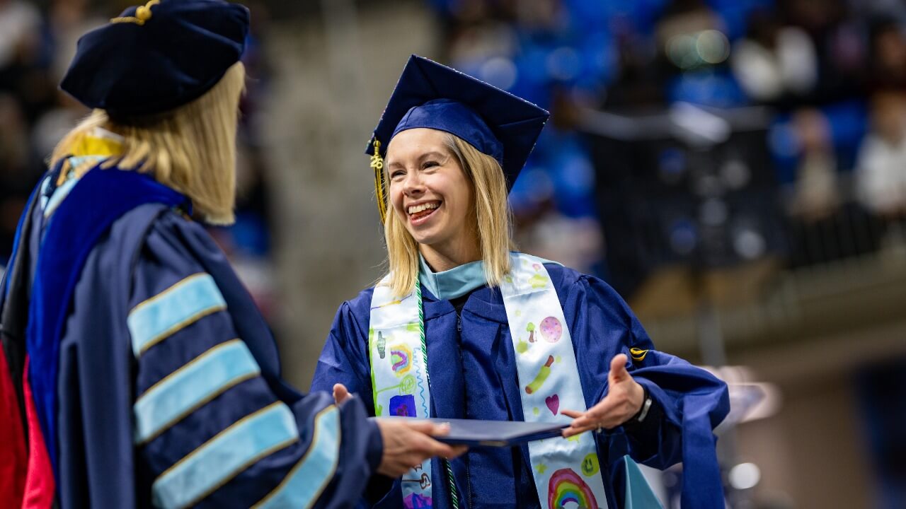 Graduate walks across stage with decorated shawl as they're greeted by President Hardin