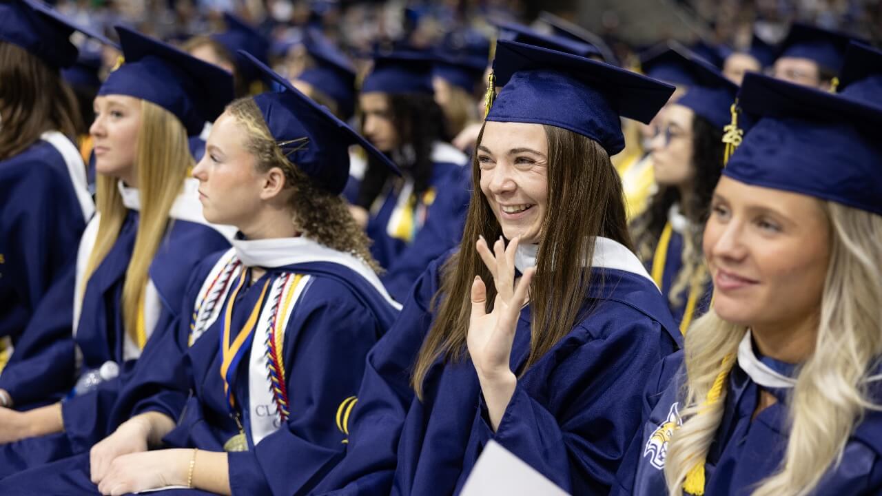Graduate smiles and waves during Commencement ceremony