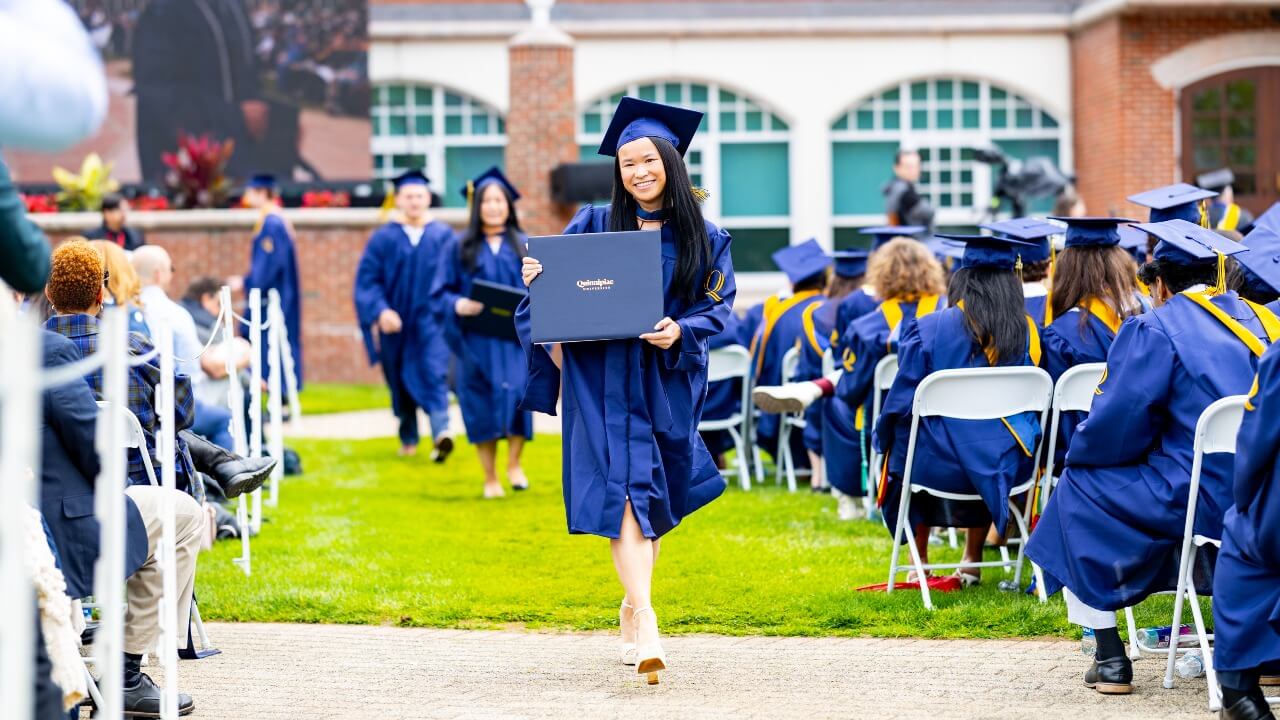 Graduate walking down aisle of chairs and holding up their diploma