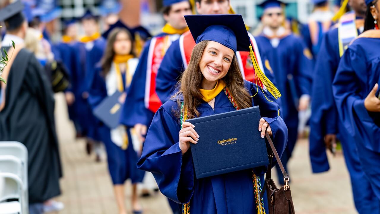 Graduate smiling and holding up their diploma with both hands