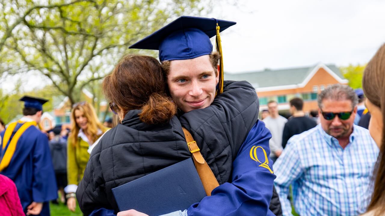 Graduate hugging loved one and smiling over their shoulder