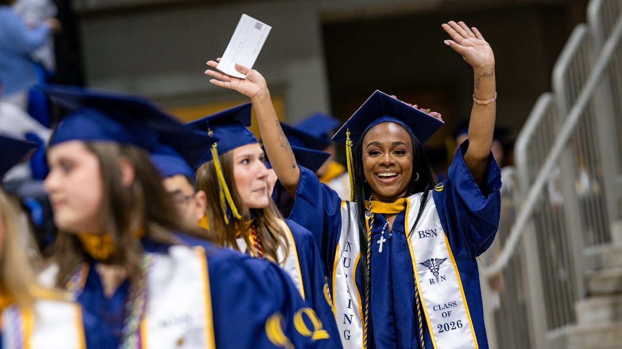 Graduate in procession line waving both hands in the air