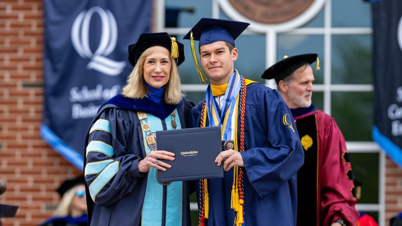 President Marie Hardin and graduate holding up diploma and smiling