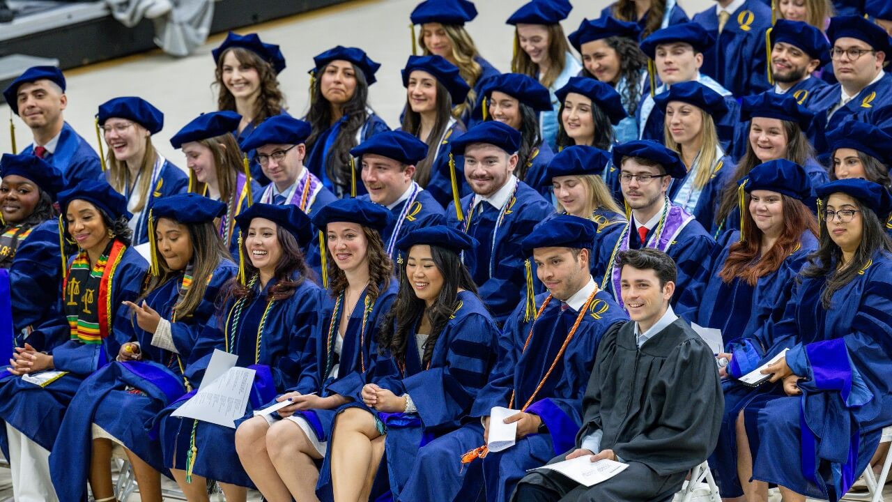 Graduates sitting down smiling at their Commencement