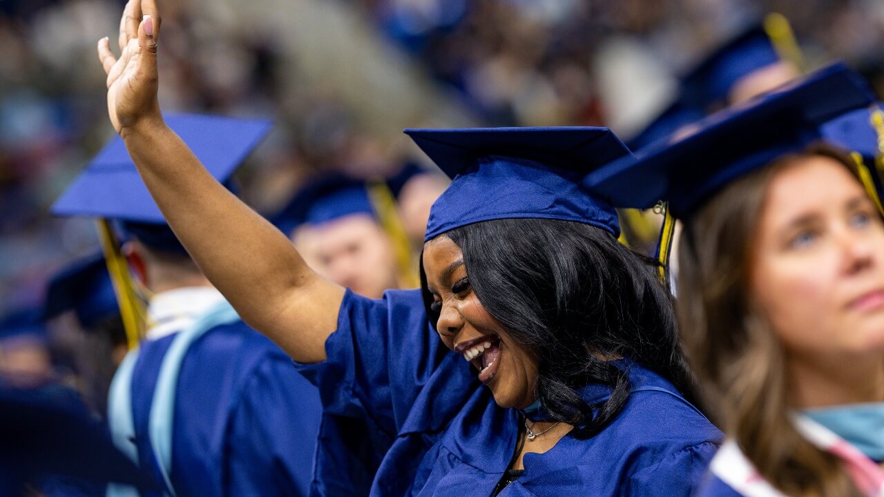 Graduate in the crowd with her hand in the air while smiling