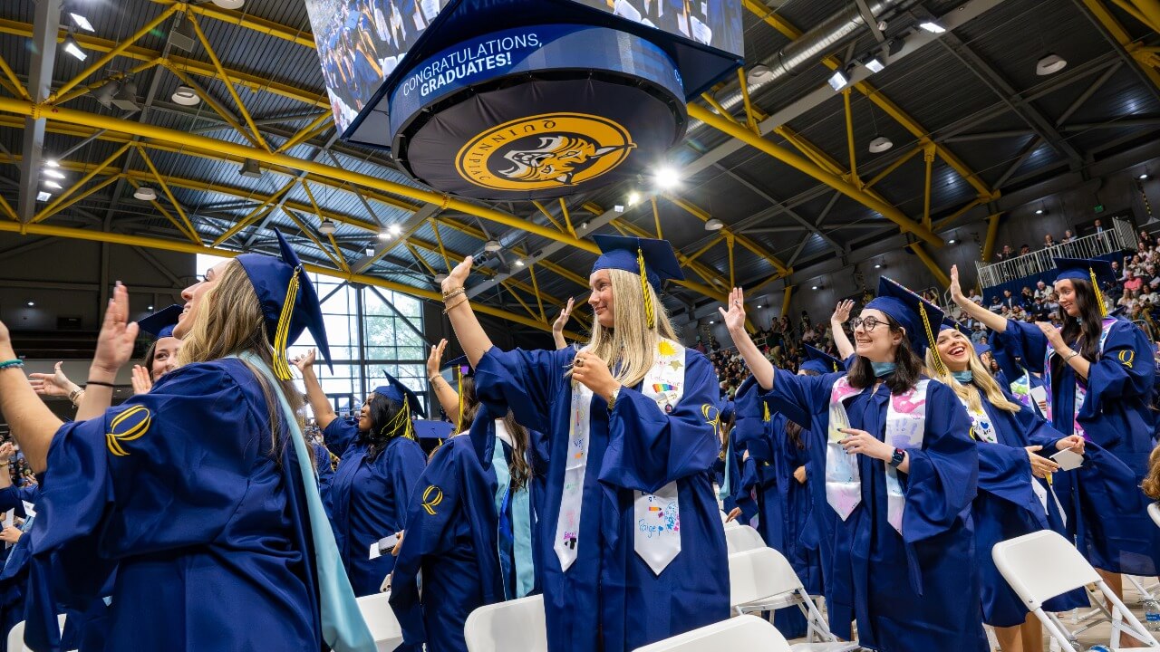 Graduates standing and waving to the guests in the crowd