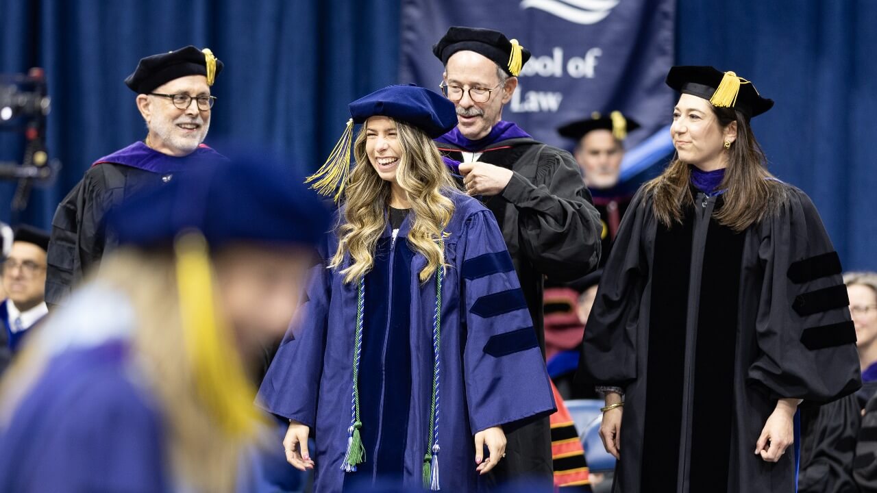 Graduate laughs on stage as they receive their hood.