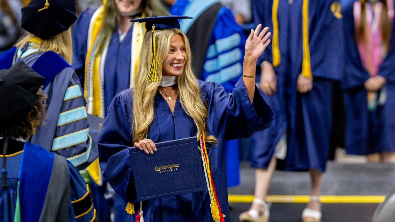 Graduate waves to audience as holding their diploma
