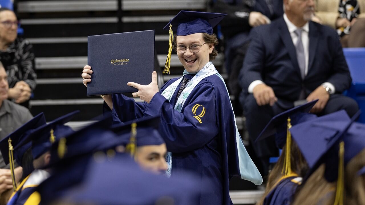 Graduate in cap and gown smiling and holding diploma