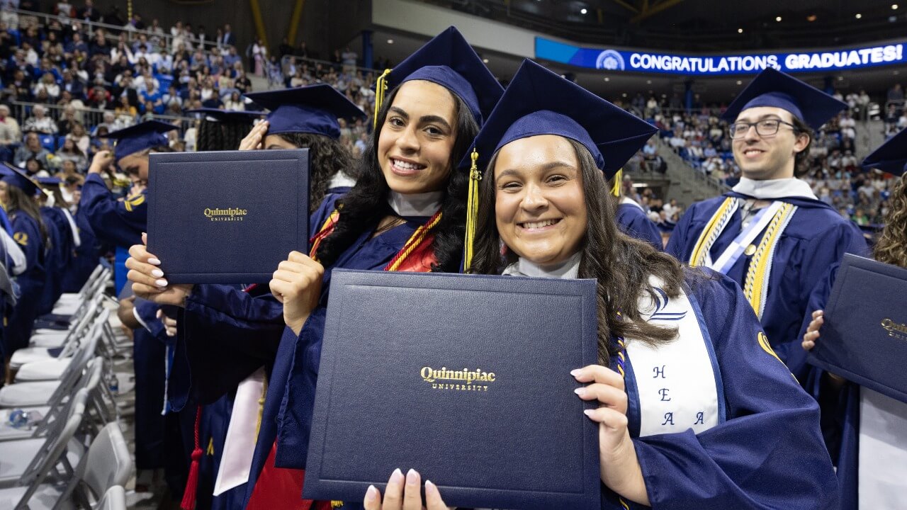 Two graduates holding up their diplomas together for a photo