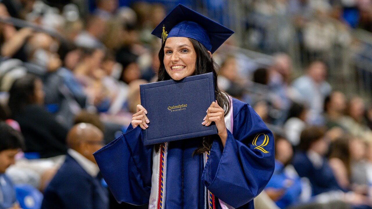 Graduate holds diploma up to face while expressing excitement