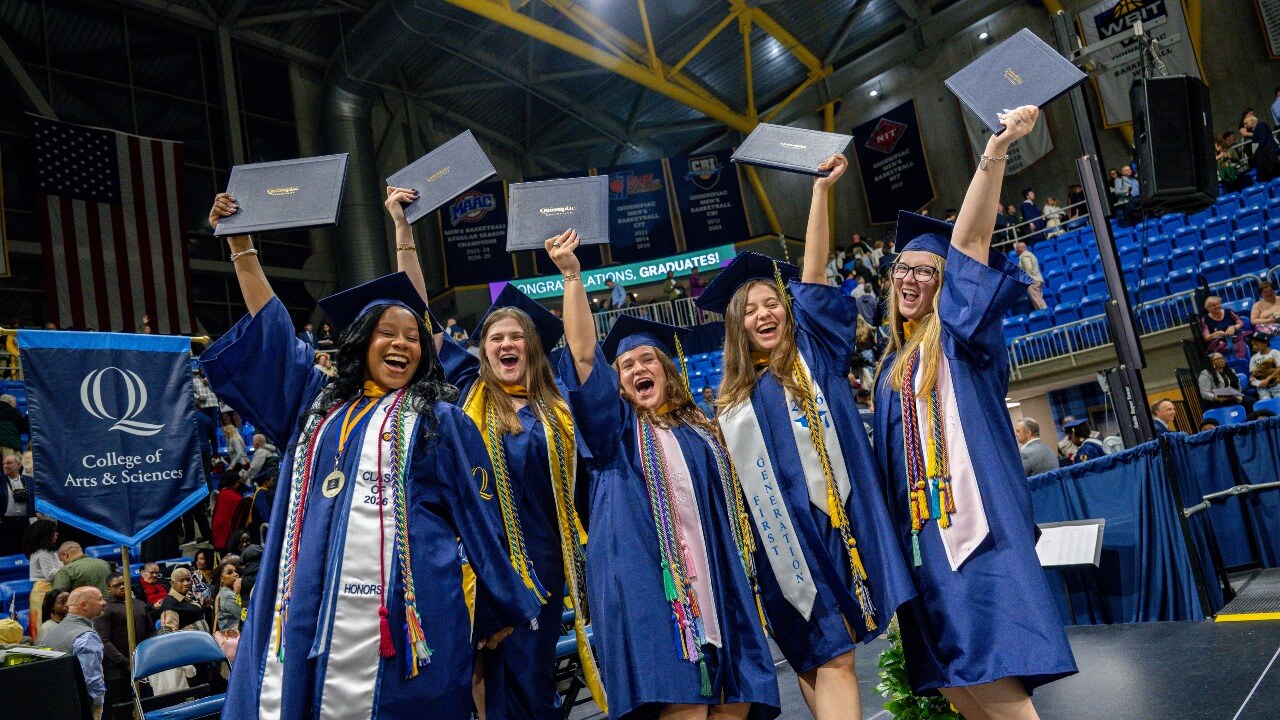 Graduates stand on stage holding their diplomas up for a photo