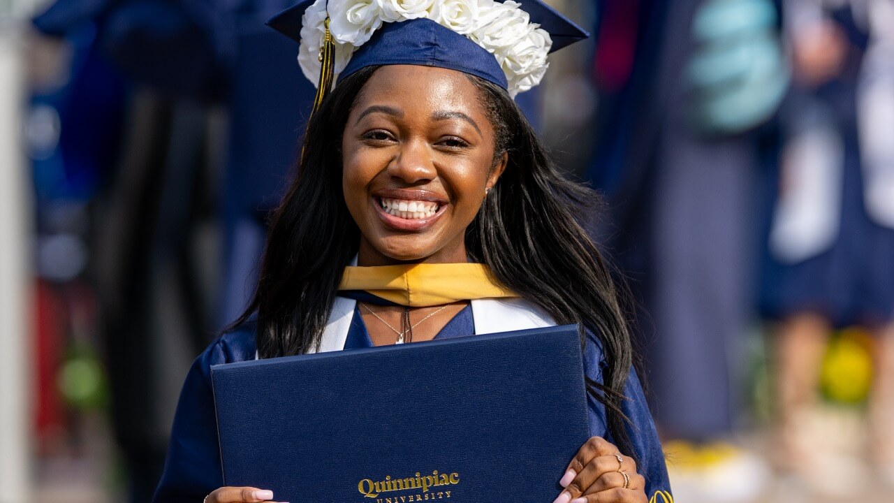 graduate in a cap decorated with flowers, smiling and holding their diploma