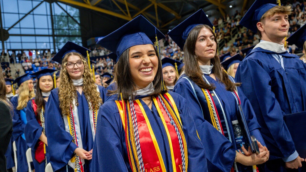 Graduates stand in audience together wearing their cap and gowns during commencement ceremony