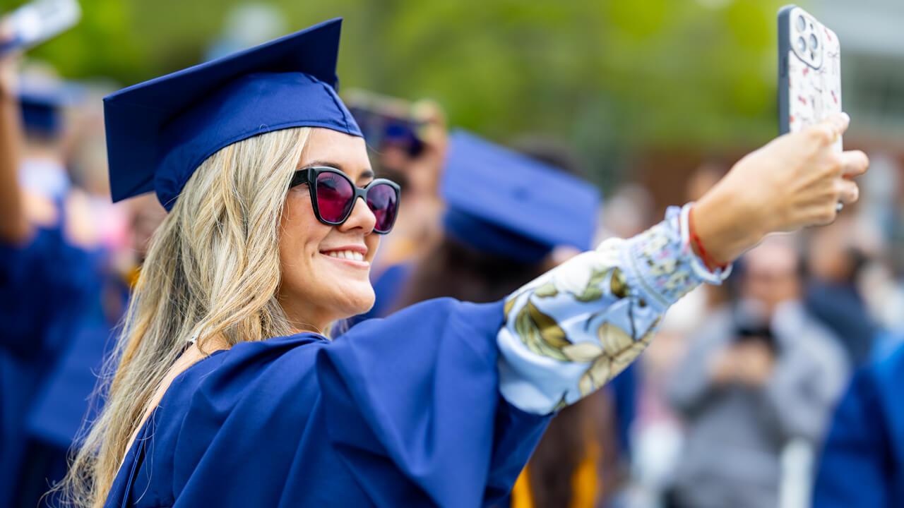 A graduate in rose-tinted sunglasses takes a selfie