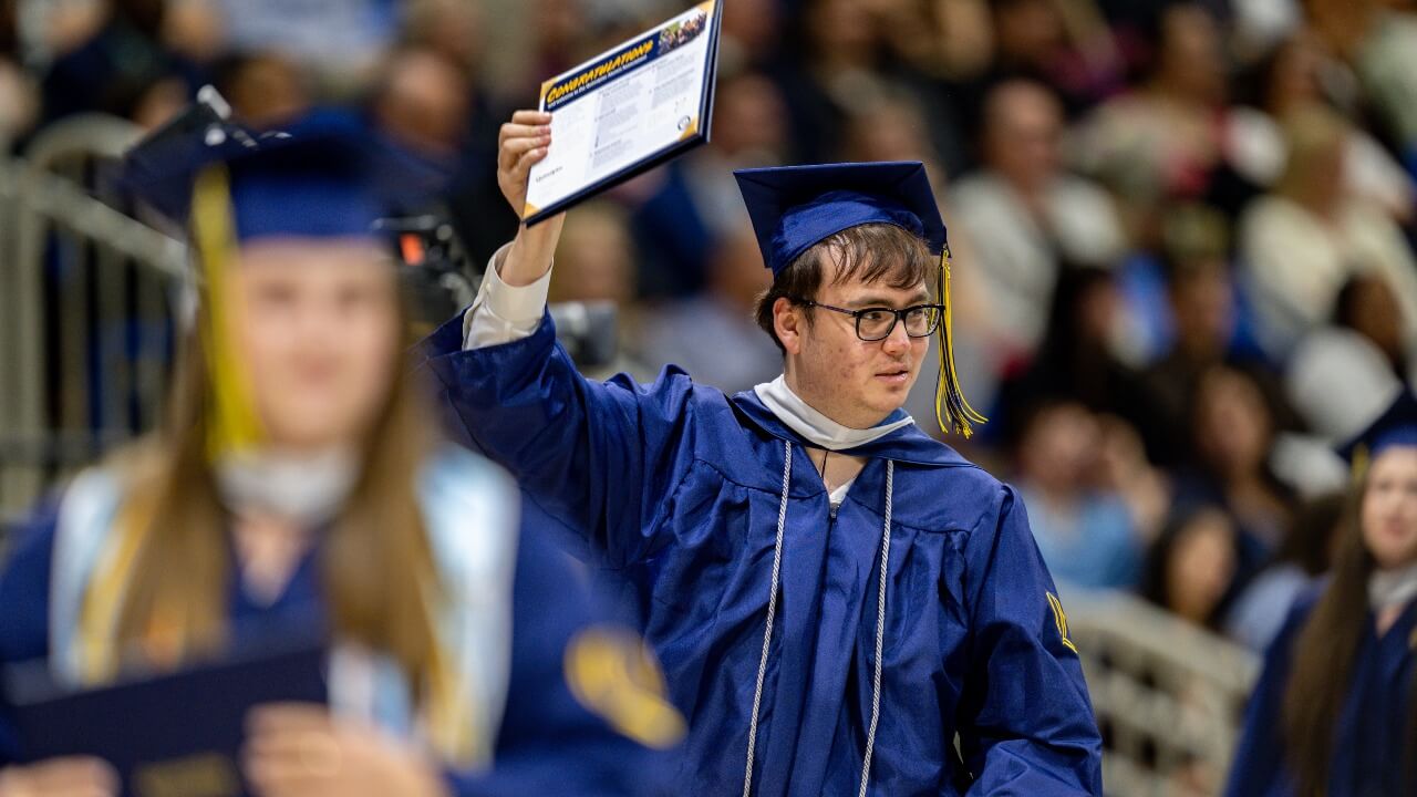 Graduate looking to the right and holding up diploma with one hand