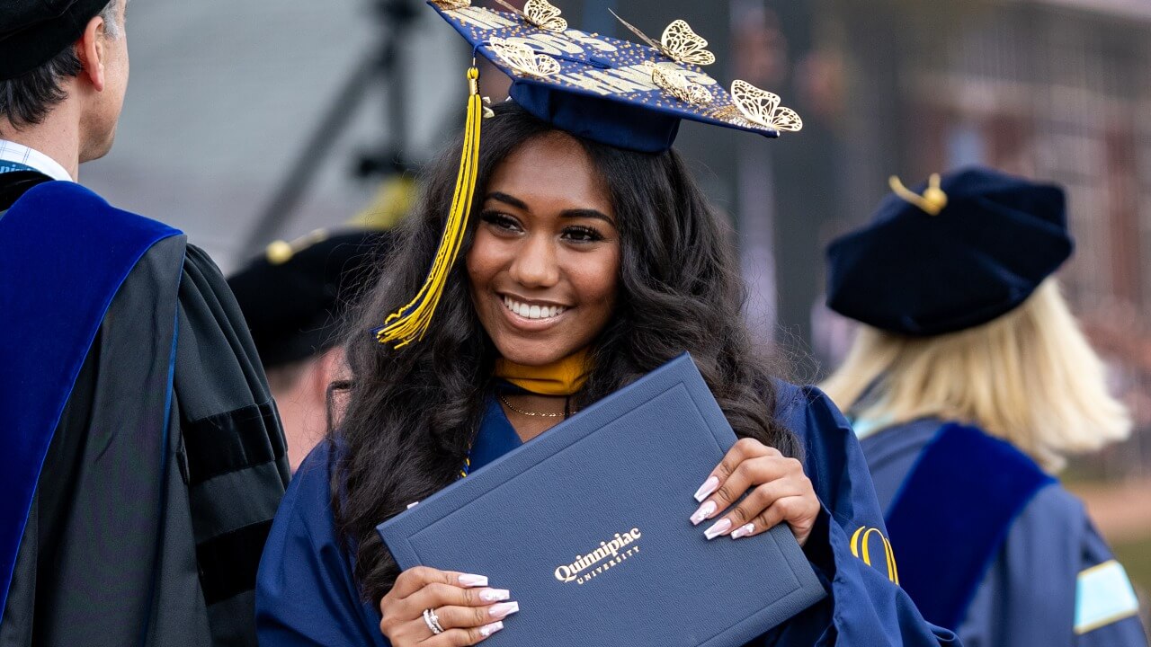 Graduate with butterflies on their cap, walking off the stage and holding up their diploma