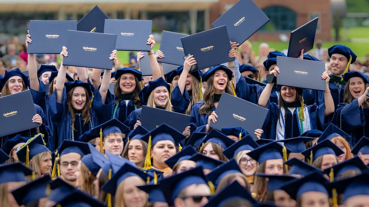 Graduates in the crowd cheering and raising their diplomas in the air