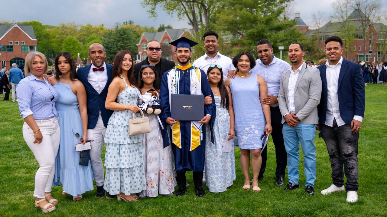 Graduate surrounded by family while holding up their diploma and smiling