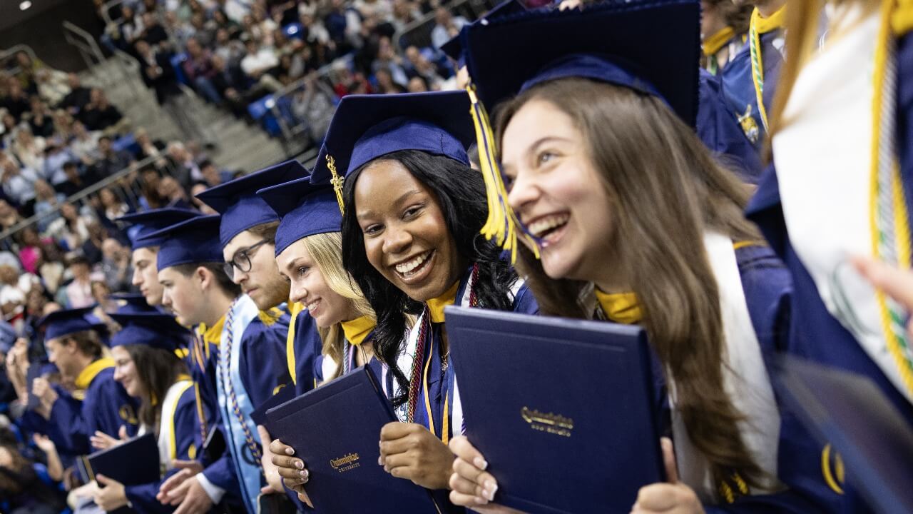 Graduates sitting in the audience holding up their diplomas