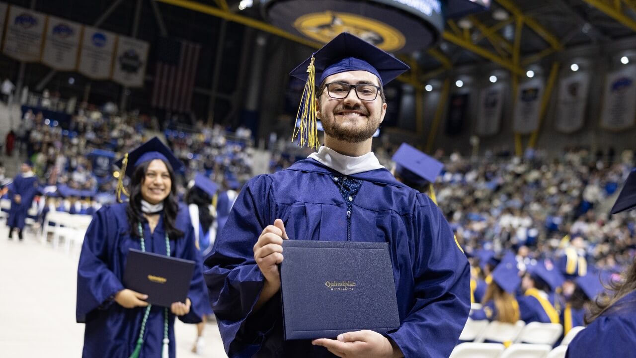 Graduate holding up their diploma and smiling for the camera