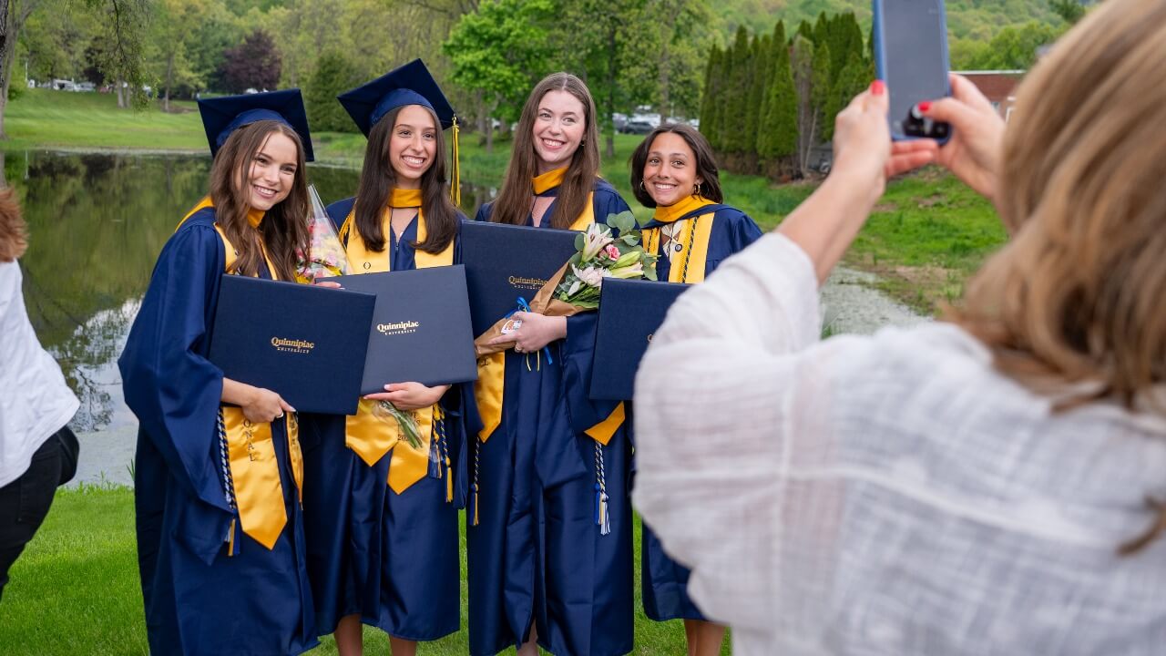 Person taking a photo of four graduates smiling next to each other