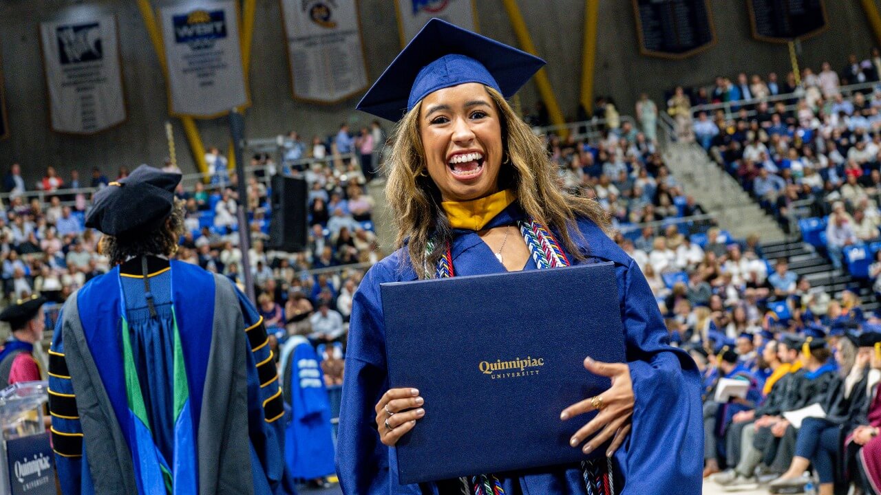 Graduate in cap and gown smiles with their degree.