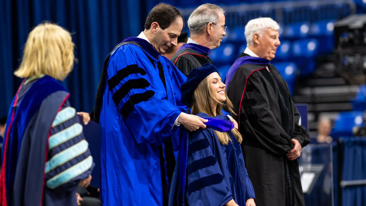 Faculty member places hood over graduate.