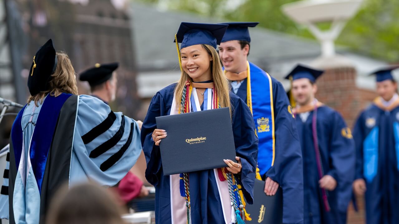 graduate smiling and holding the diploma, posing for a photo