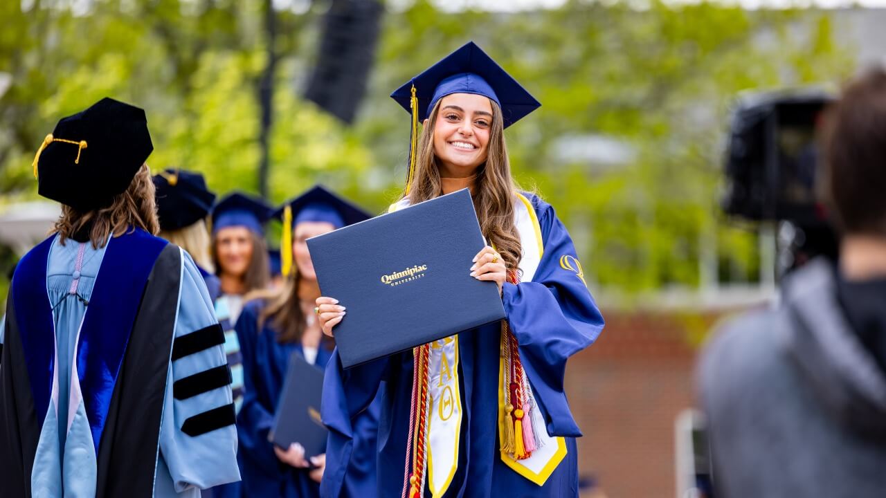 Graduate holding up their diploma and smiling to the camera