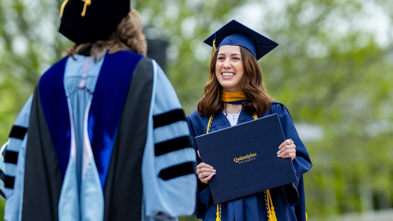 graduate smiling and posing for a photo, while holding a diploma