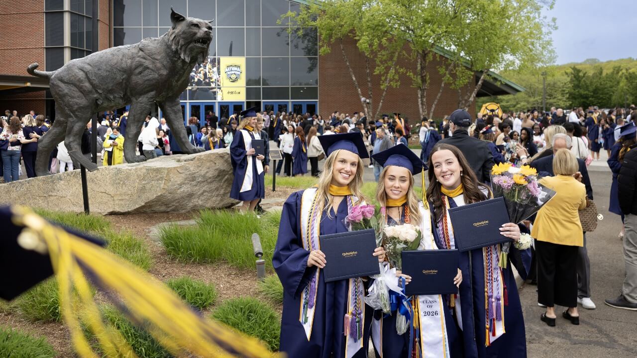 Three graduates posing for a photo in front of the Bobcat Statue outside of the M&T Bank Arena