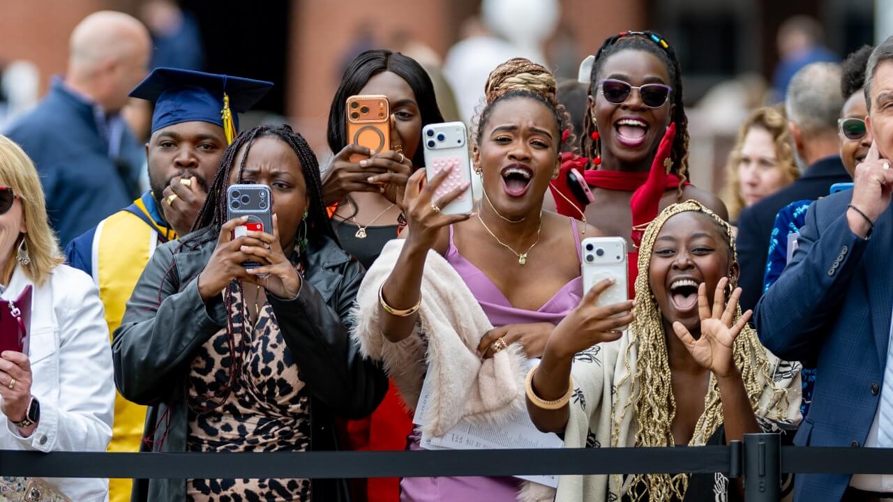 the audience standing up in the crowd with their phones out and are taking photos of their graduates