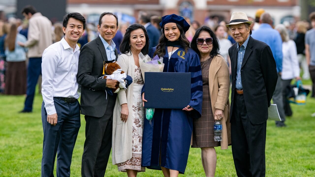a happy Quinnipiac family smiling with their graduate in the middle holding their diploma