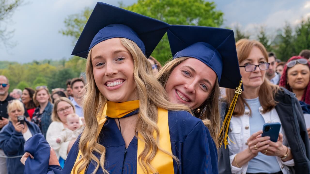 a graduate playfully peeking behind the shoulder of another happy graduate