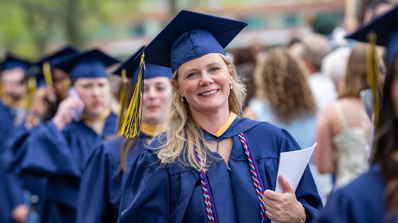 in a line of graduates walking to their seats, one smiles and looks at the camera