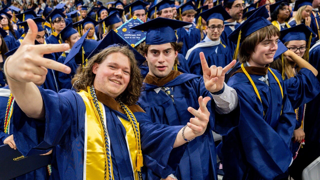 Graduates posing and hold up a peace sign in their regalia