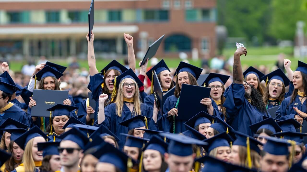 Graduates in caps and gown cheer in the crowd holding up their degrees.